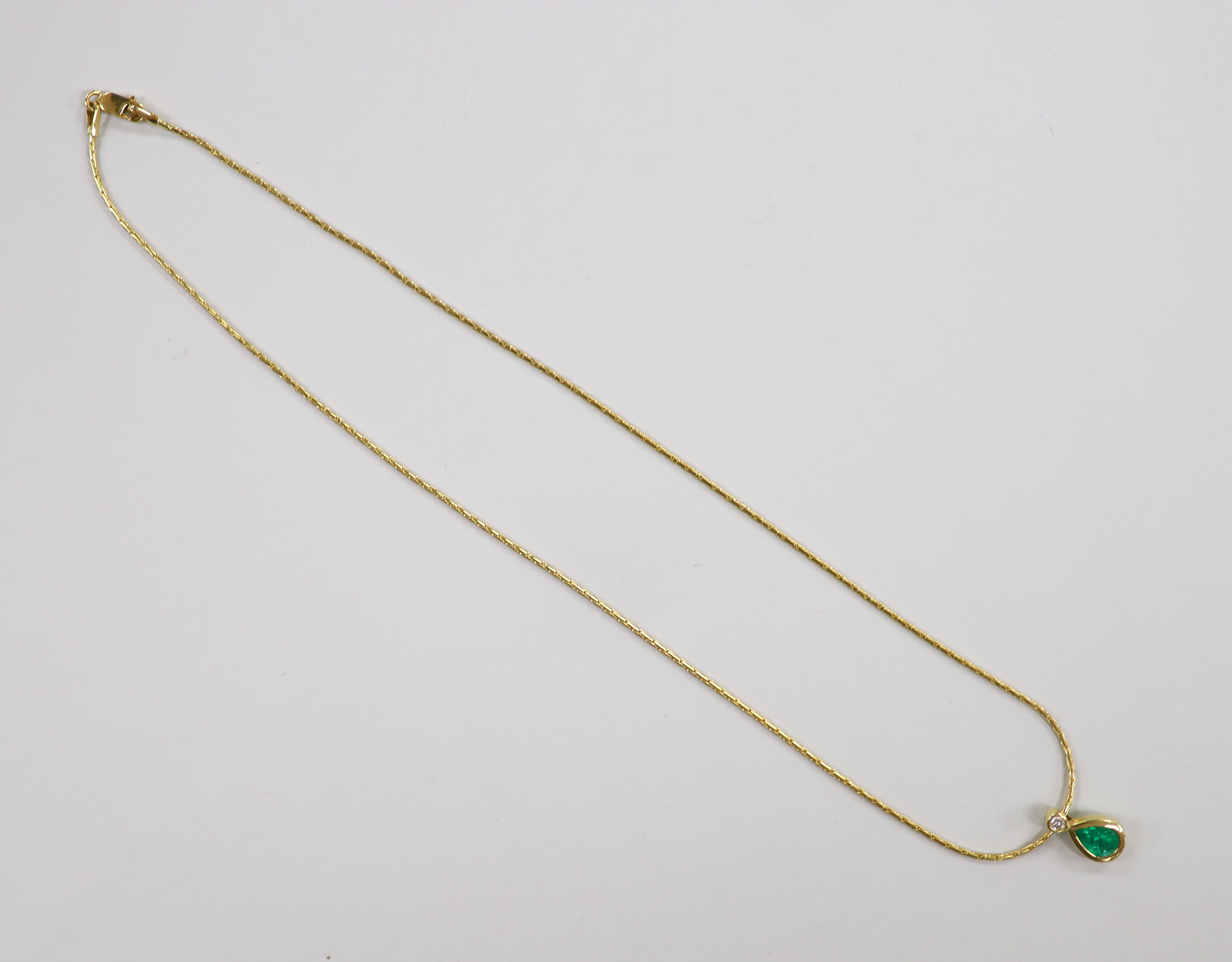 A modern 18ct gold, pear cut emerald and round cut diamond set pendant, 14mm, on an 18ct gold chain, 38cm, gross weight 6.3 grams.